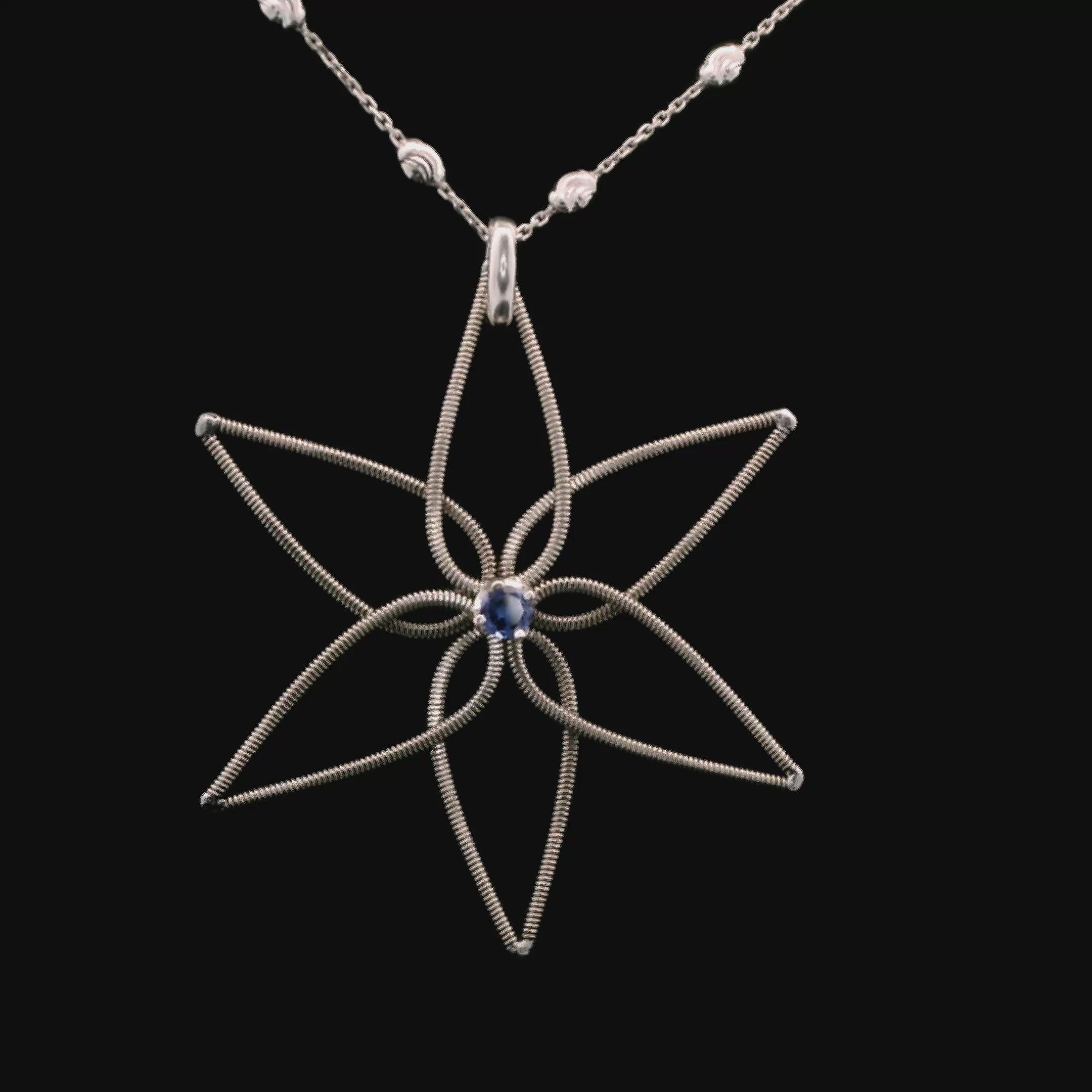 Electric guitar string flower pendant with a blue gemstone on a chain, rotating on a black background