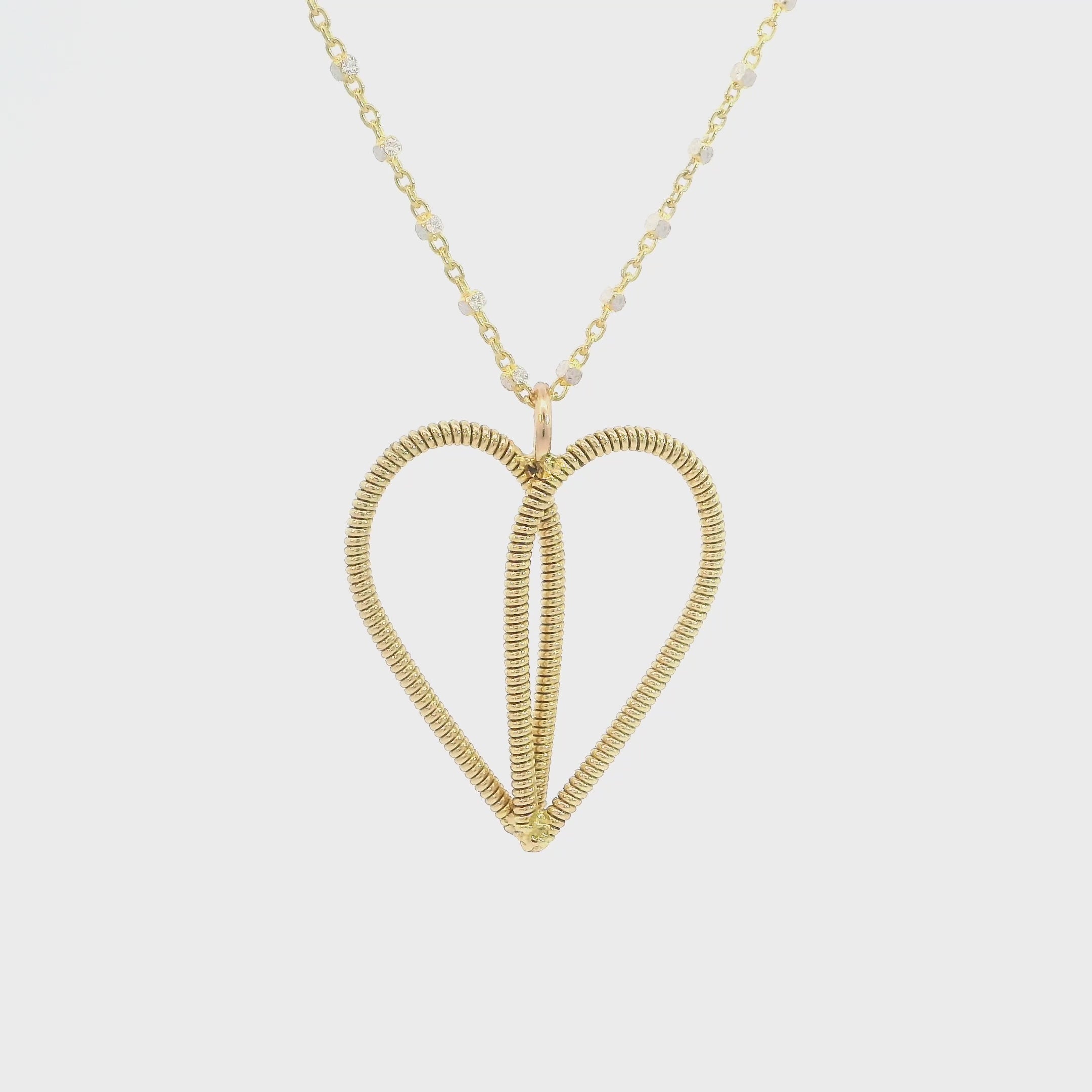 Gold guitar string heart necklace rotating on  a white background