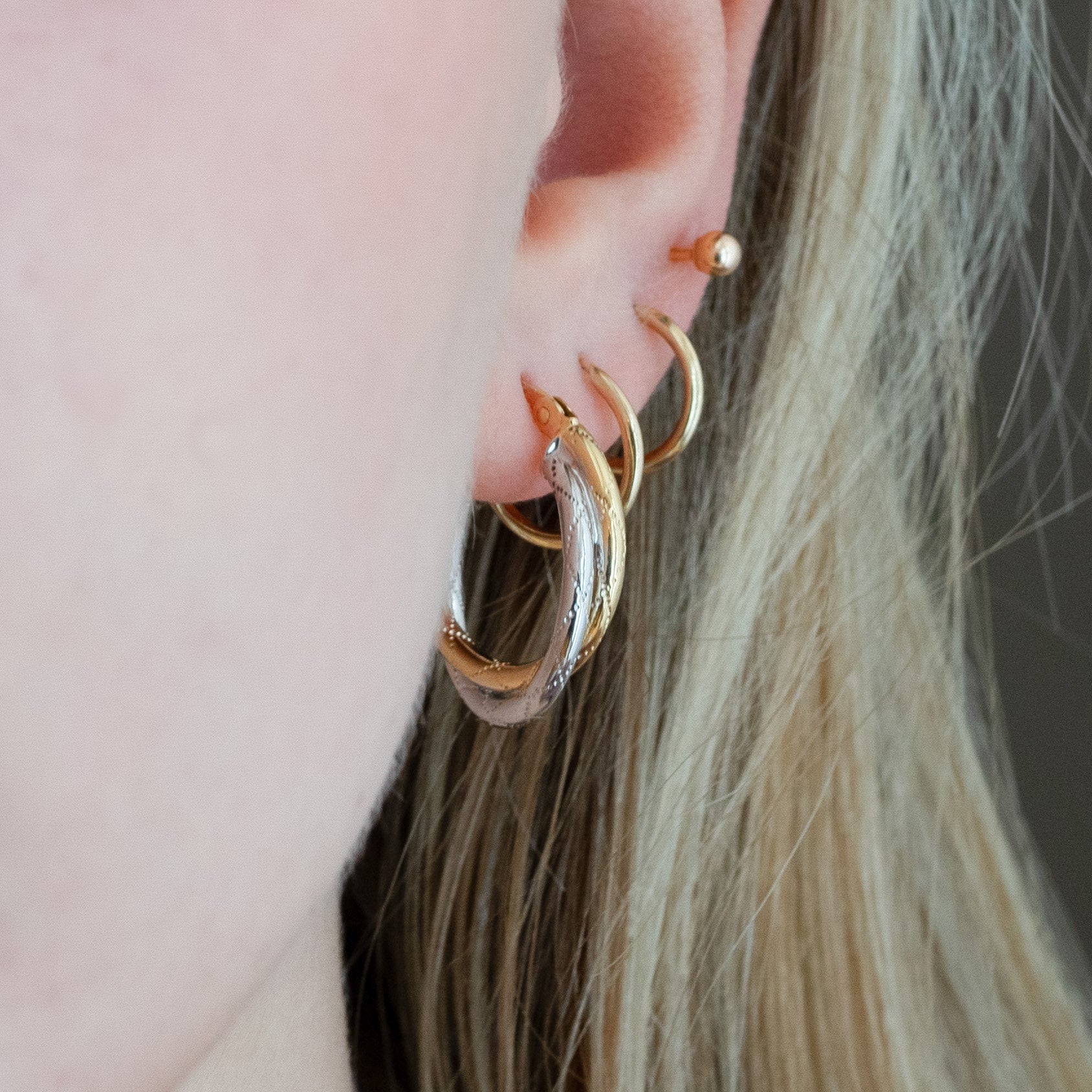 Close-up of an ear wearing gold hoop earrings with a blurred background