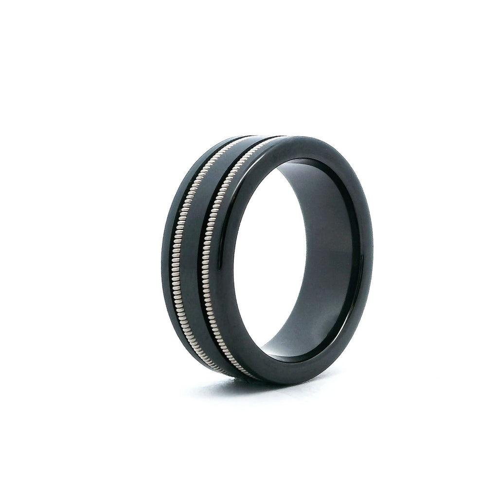 Side view of a black ceramic ring with two guitar strings embedded on a white background 