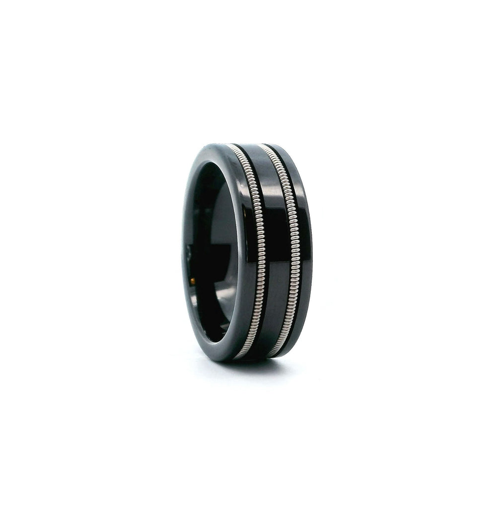 front view of a black ceramic ring with two guitar strings embedded on a white background 