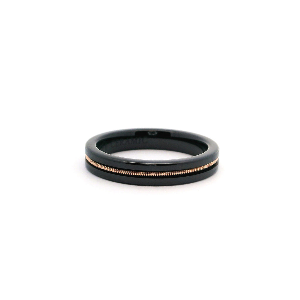 Black ring embedded with bronze guitar string laying on a white background