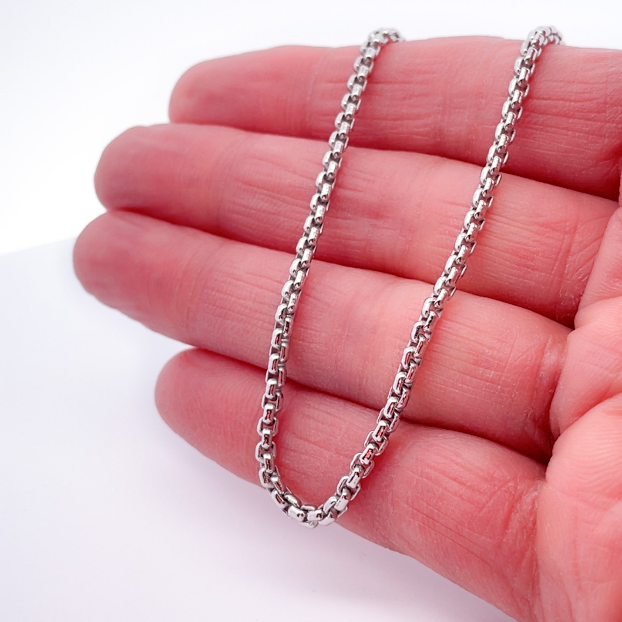 Silver rounded box chain on hand with white background.