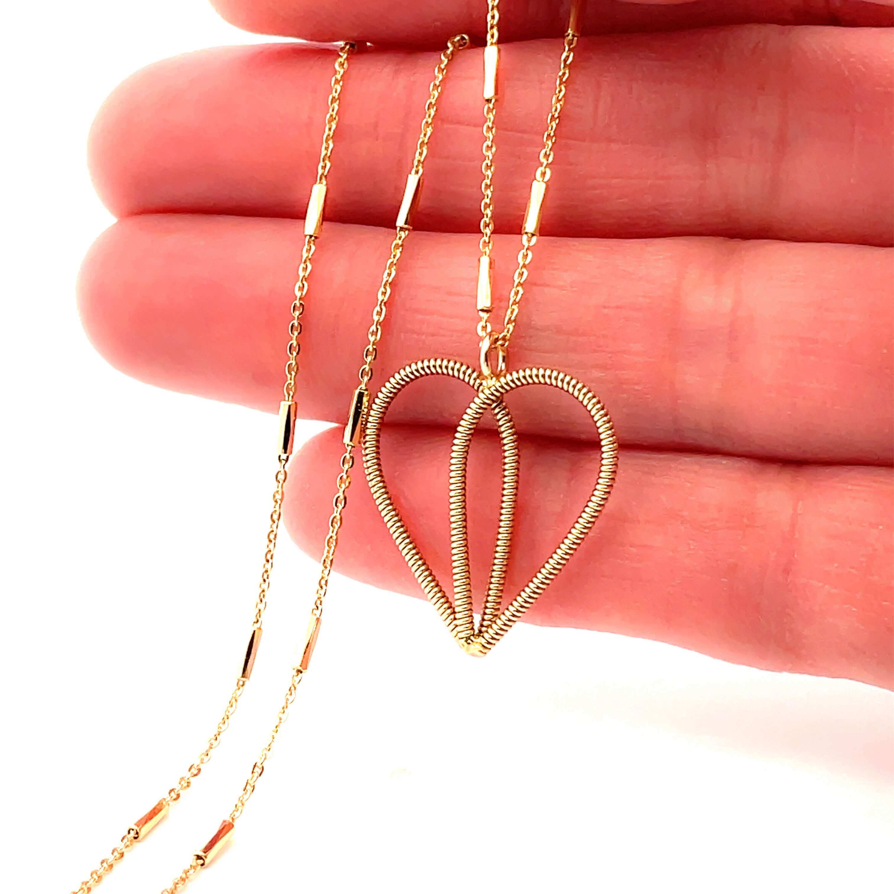 Gold guitar string heart necklace on hand.