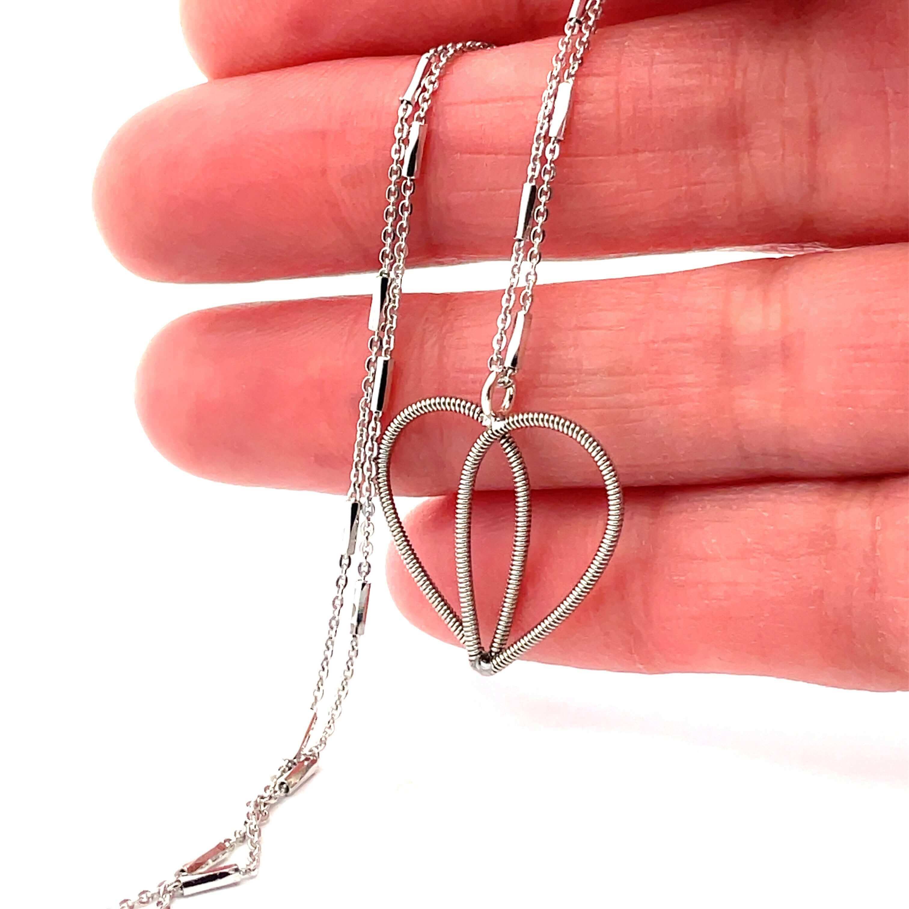 White gold guitar string heart necklace on hand.