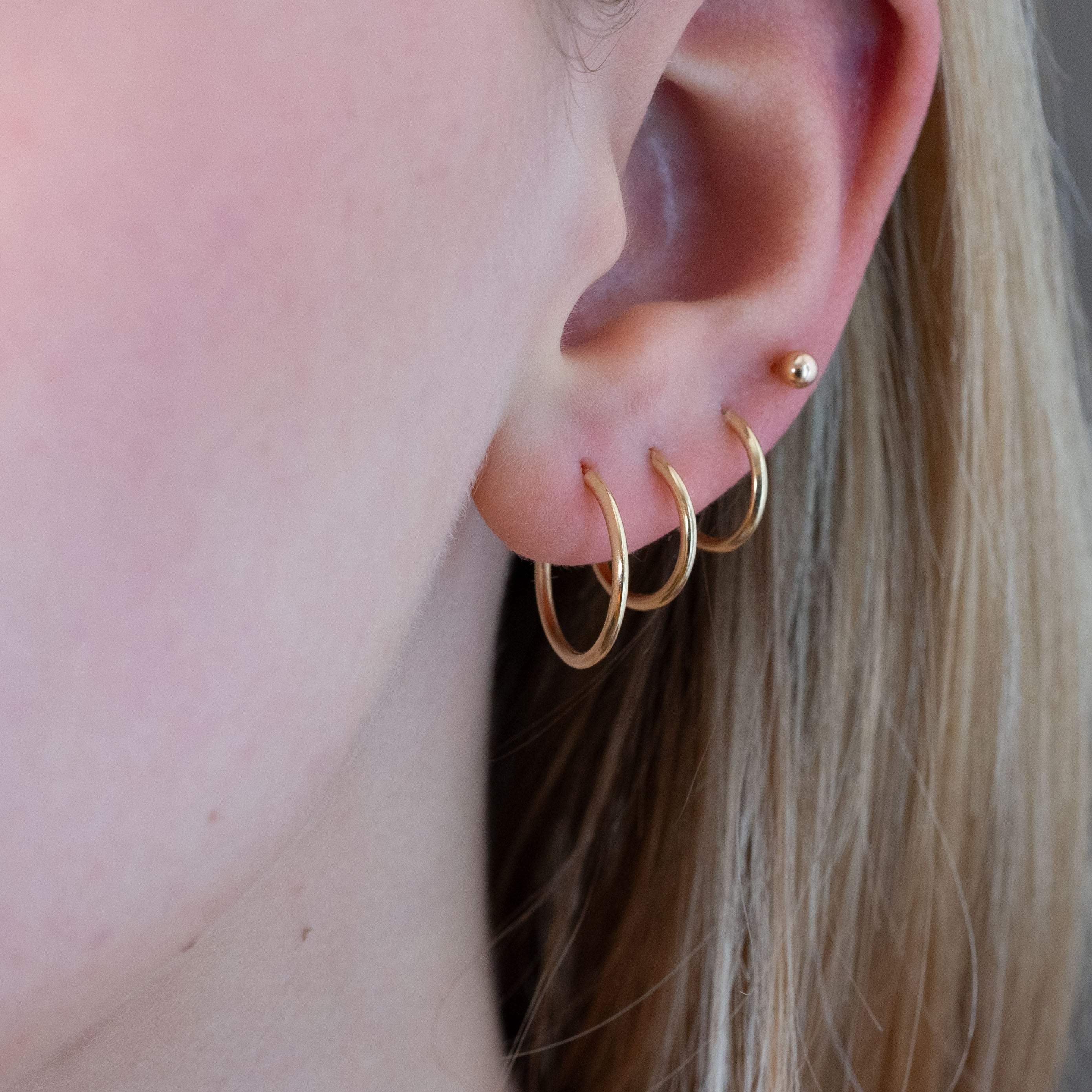 model wearing 3 stacked small gold hoop earrings