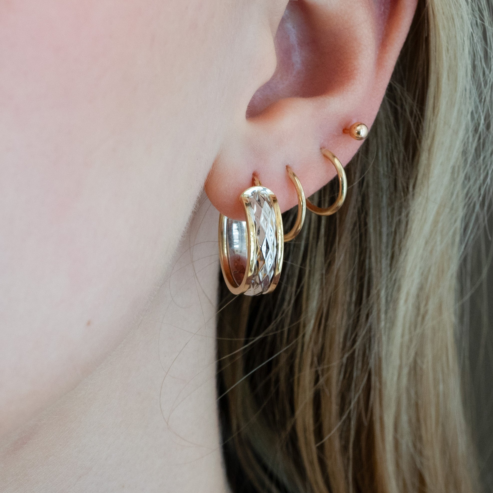 Close-up of an ear wearing gold hoop earrings with a blurred background
