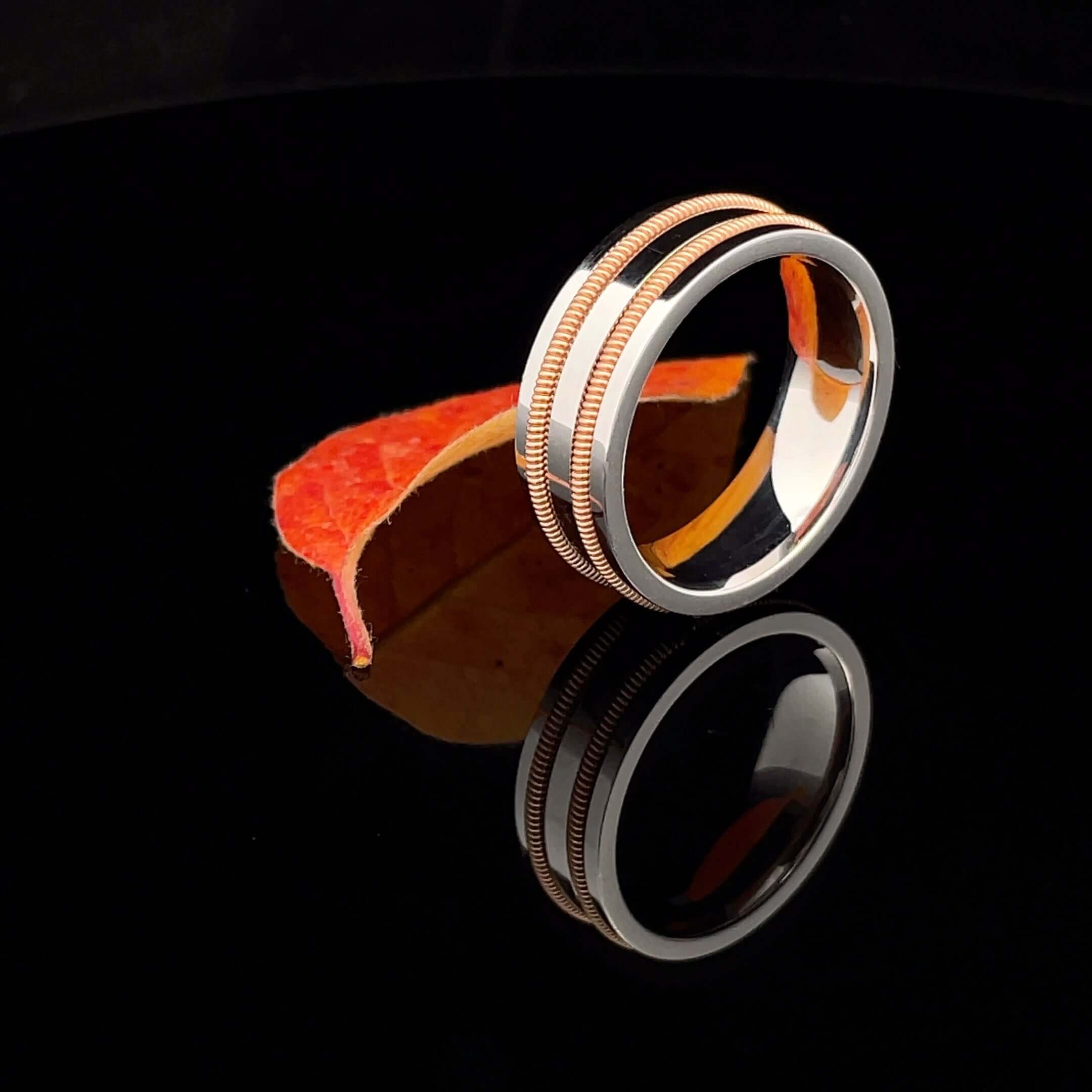 White gold ring with two guitar strings embedded on black background with orange leaf.