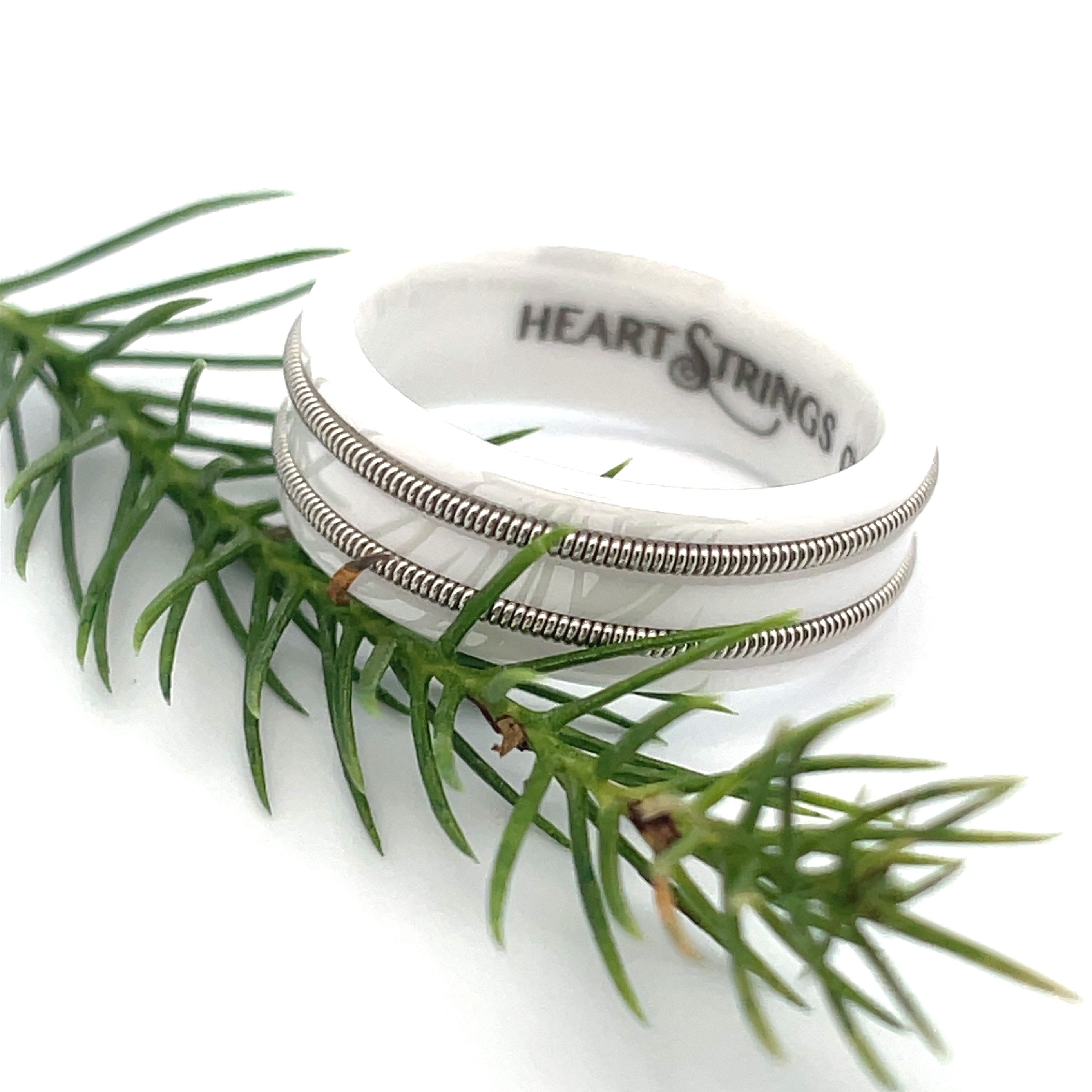 White ring with embedded electric guitar string resting on an evergreen twig on white background.