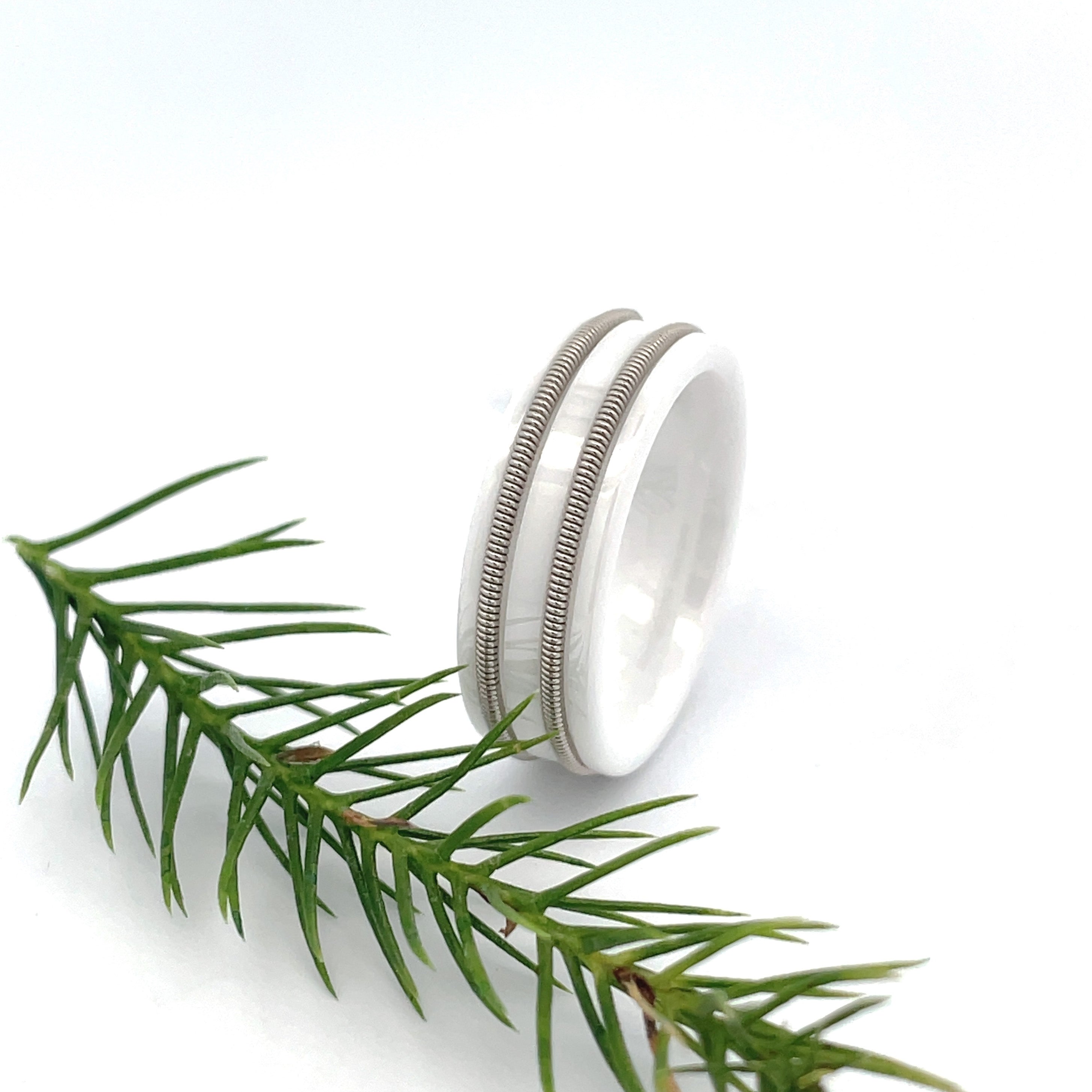 White ring with embedded electric guitar string standing next an evergreen twig on white background.