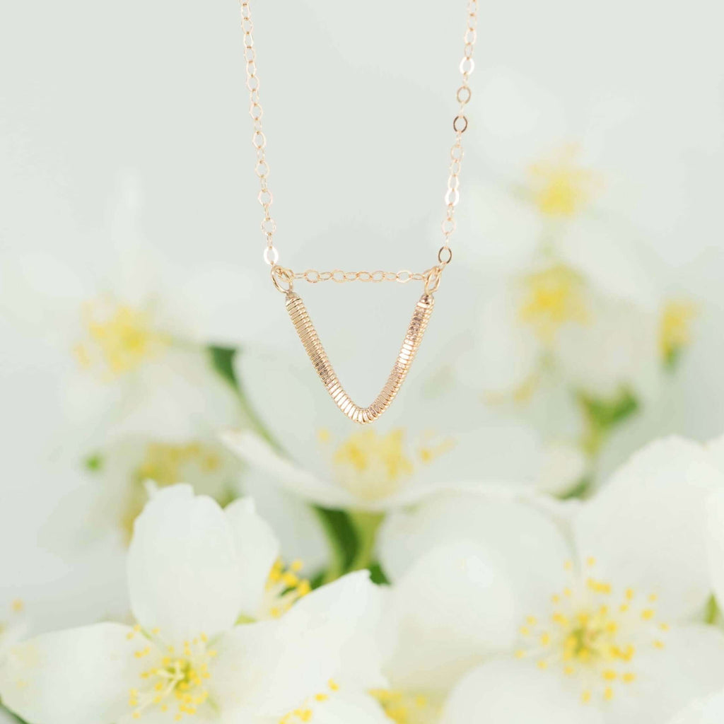 Rose gold guitar string v-necklace hanging with flowers in the background