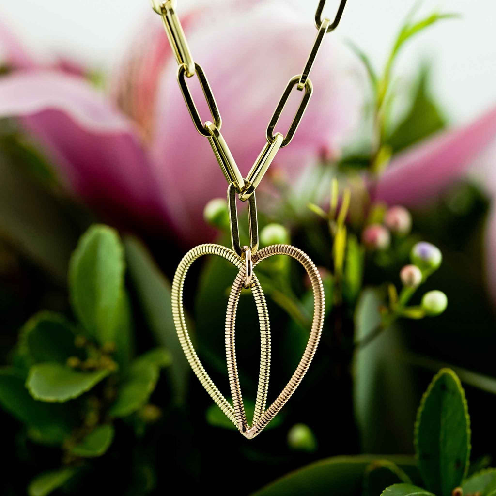 two-toned hanging acoustic guitar string heart pendant on a 14K gold long link chain on a flower background