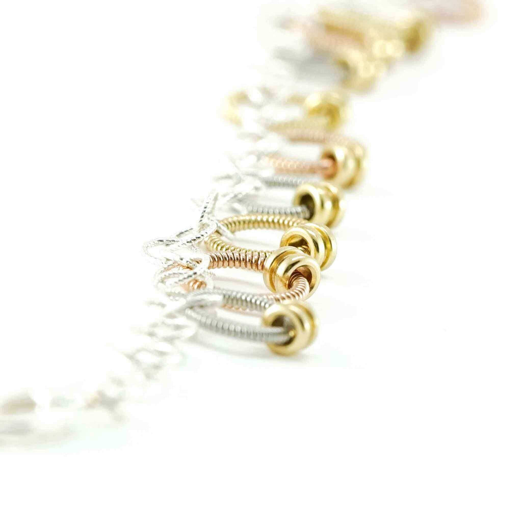 bracelet made of small rings of guitar string and ball ends laid out on a white background