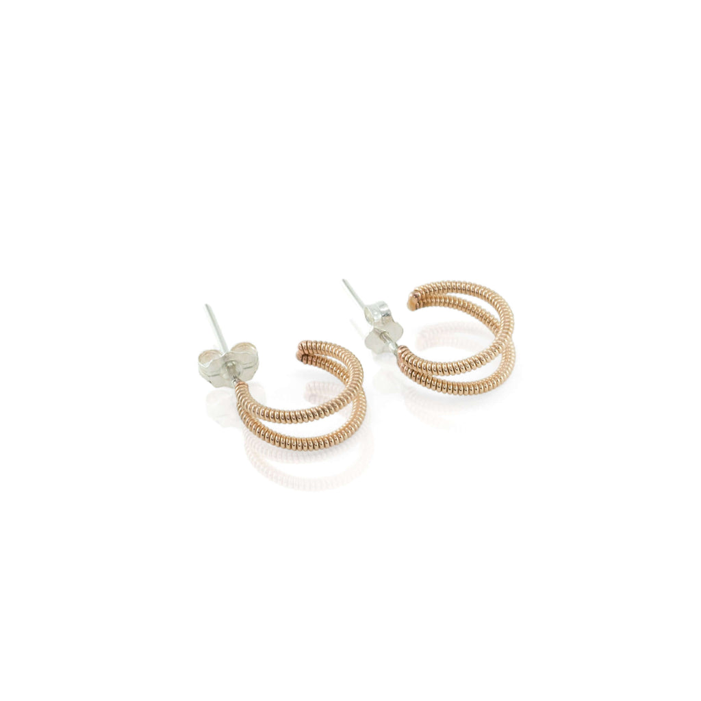 small crescent shaped acoustic guitar string huggie earrings on a white background