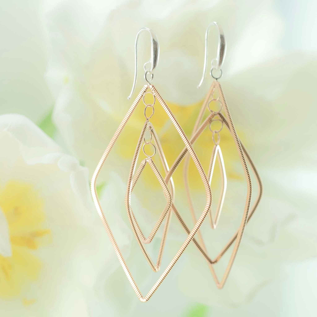 floating diamond-shaped dangling guitar string earrings with silver ear hooks and white tulips in the background
