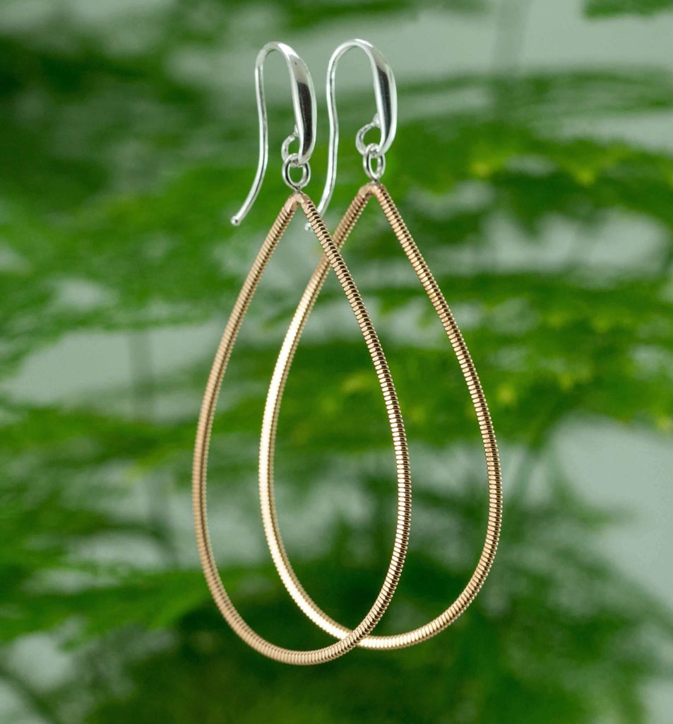 Guitar string drop earrings with silver ear hooks with green plant in the background