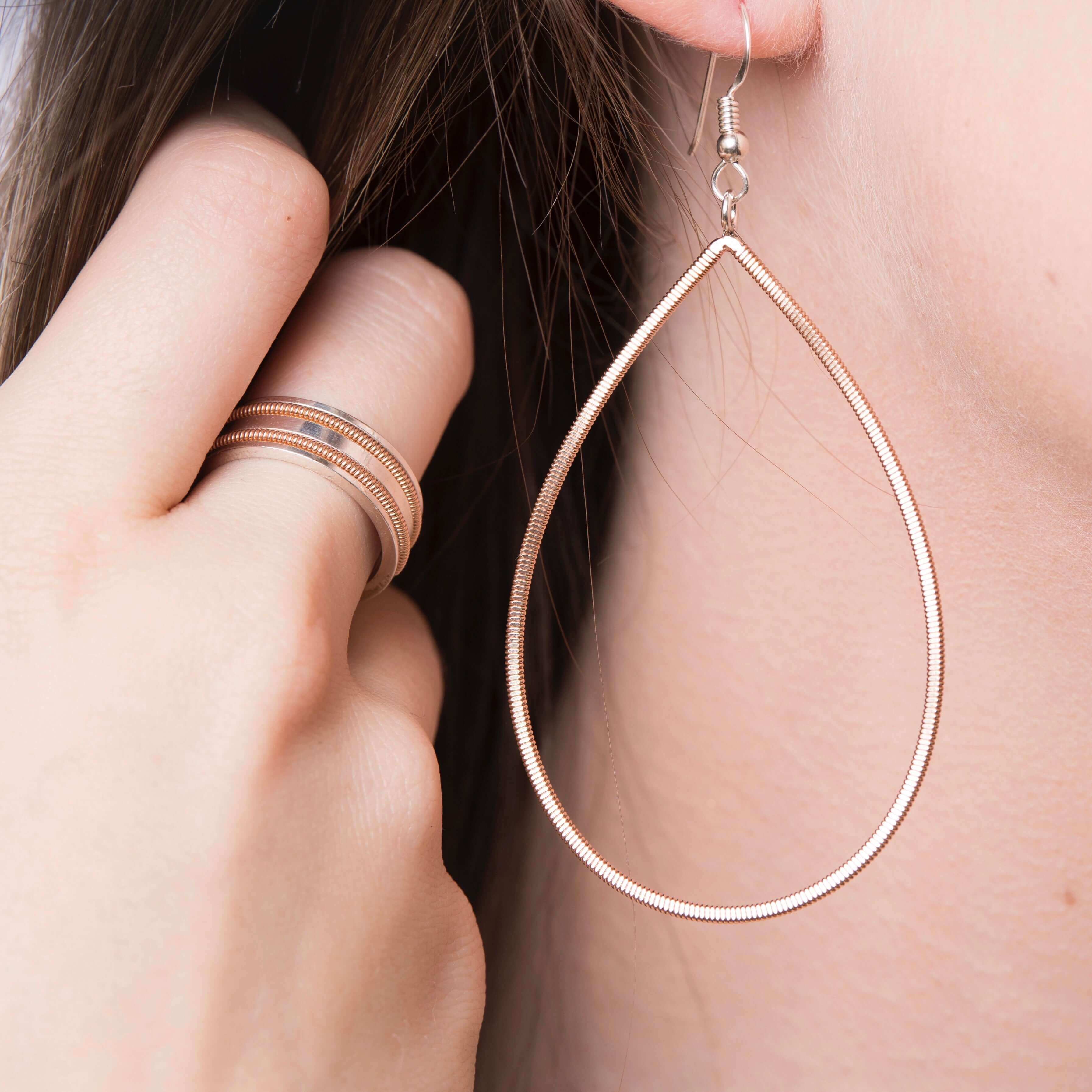 Close up of model wearing guitar string drop earring and guitar string silver ring