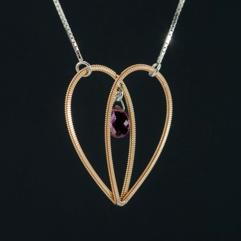 Acoustic guitar string heart pendant with a garnet gemstone suspended in the centre on a silver box chain on a black background