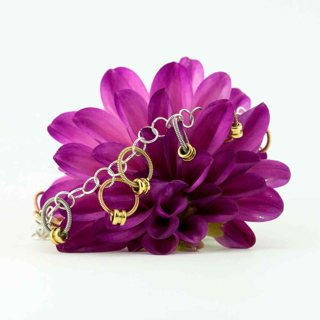 bracelet made of small rings of guitar string and ball ends on a pink flower