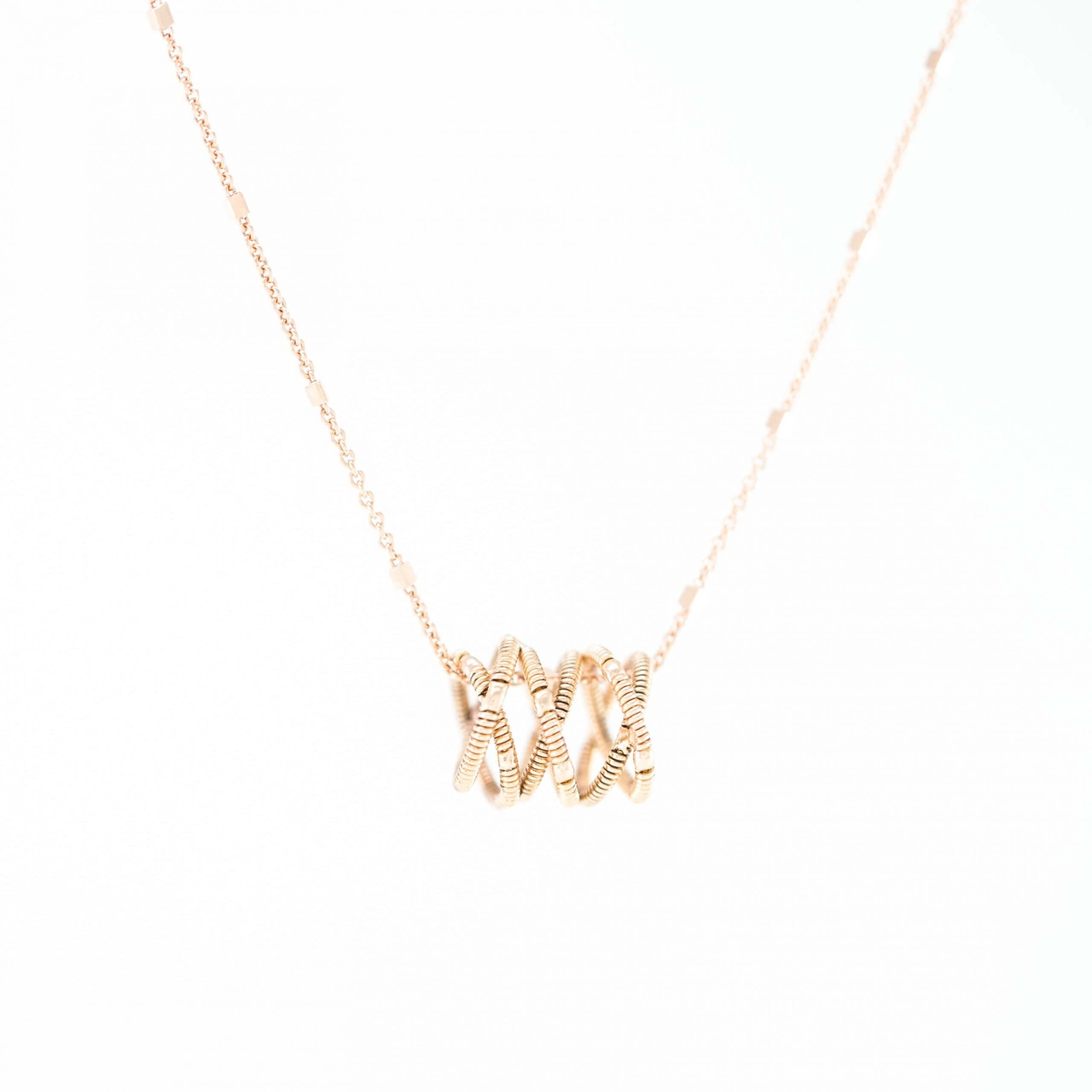 guitar string helix shaped necklace with 18k rose gold chain on a white background