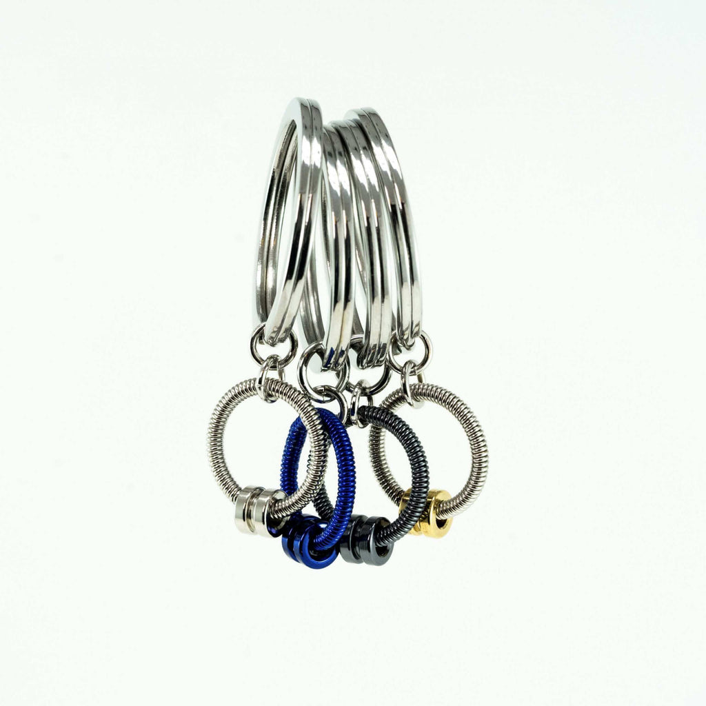 four bass guitar string keychains in silver, blue, and grey hanging with a white background