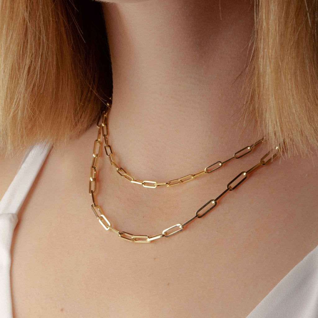 Model wearing small and medium sizes of 14k yellow gold paperclip chains and a white top.