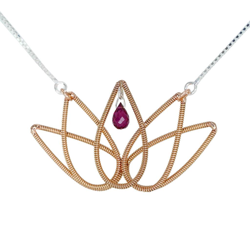 Lotus flower pendant made from reclaimed guitar string, suspended on a silver chain with a red tourmaline gemstone in the center, on a white background