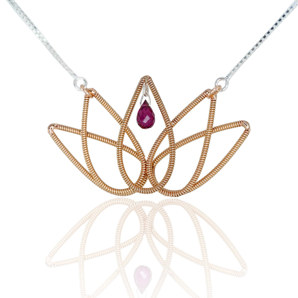 Lotus flower pendant made from reclaimed guitar string, suspended on a silver chain with a red tourmaline gemstone in the center, on a white background with reflection