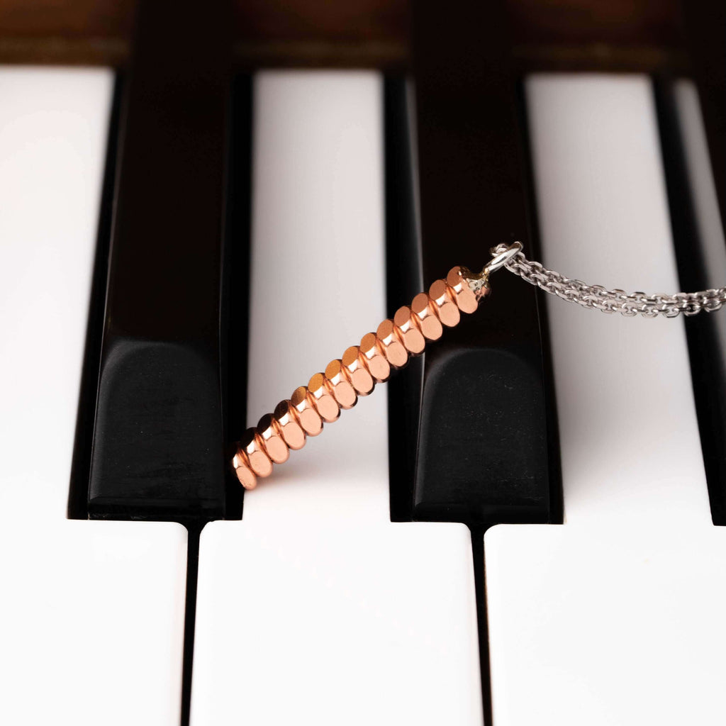 Piano string bar necklace laying across the keys of a piano