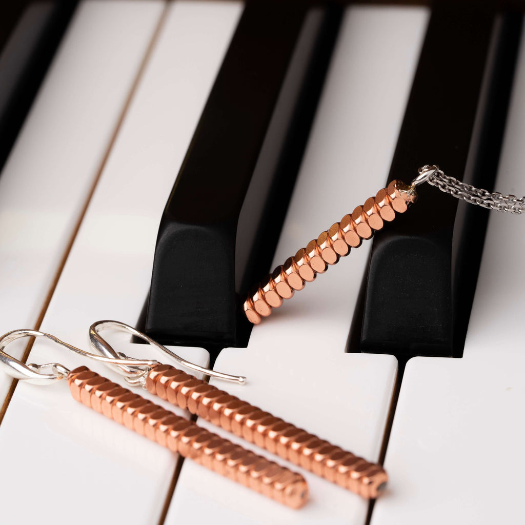 Piano string bar necklace and earrings laying across the keys of a piano