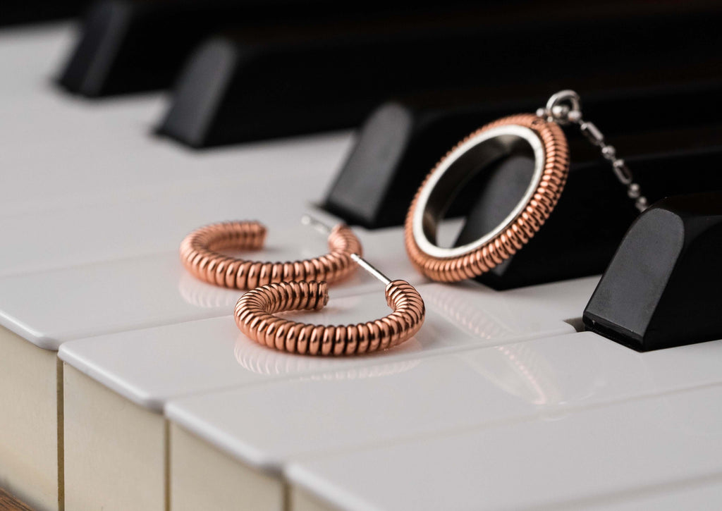 Piano string hoop earrings and piano string round pendant laying on the piano keys of a piano